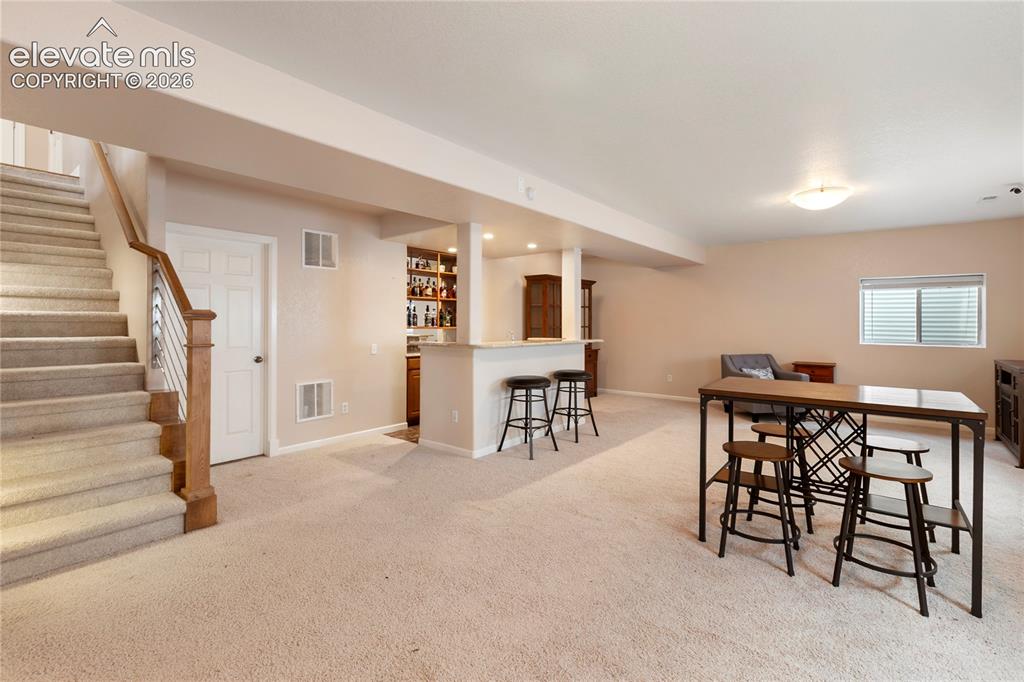 Image 22 of 38: Carpeted staircase with wood and metal railing, integrated wet bar with bui