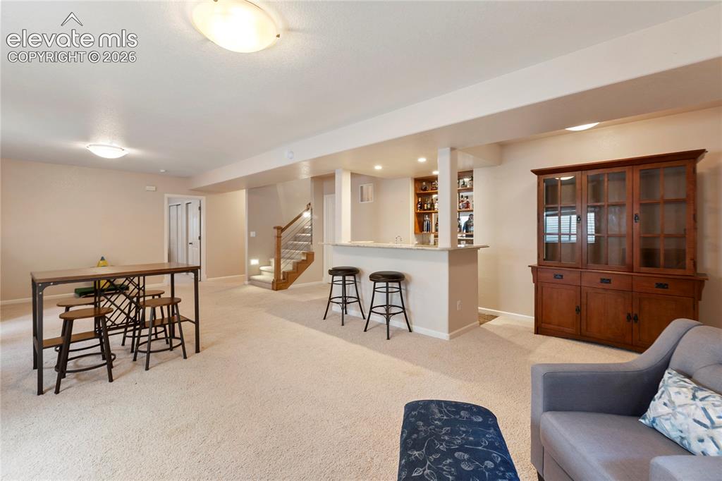 Image 23 of 38: Expansive carpeted area featuring a built-in wet bar with shelving, a woode