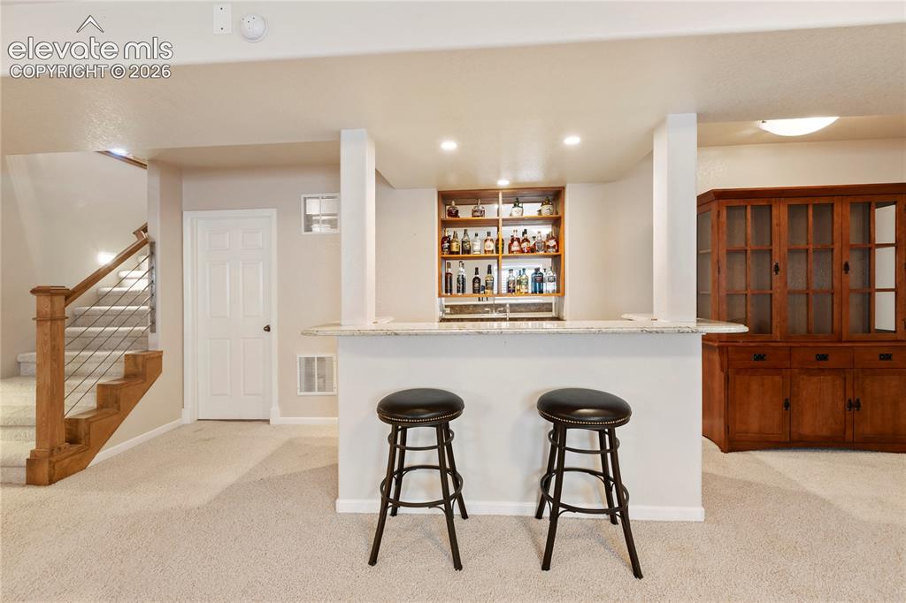 Image 24 of 38: Built-in bar with stone counter, integrated shelving, and recessed lighting