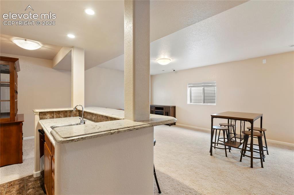 Image 25 of 38: Built-in wet bar with a single basin sink, light-toned countertop, and tile