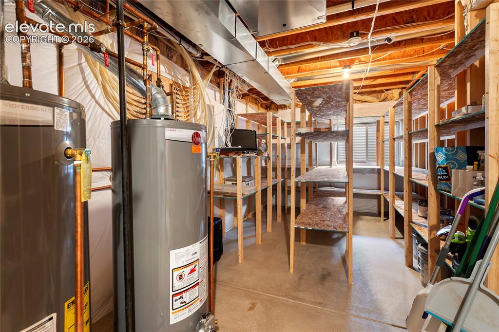Image 29 of 38: Dual water heaters, exposed wood joists, concrete flooring, and extensive b