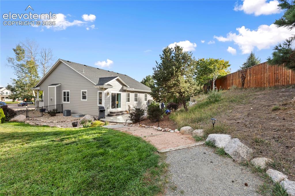 Image 35 of 38: Gray siding exterior with multiple windows, a rear patio, and a gravel path
