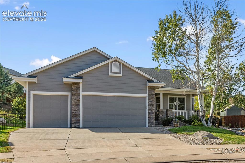 Image 37 of 38: Gray siding exterior with stone accents, featuring a two-car garage, covere