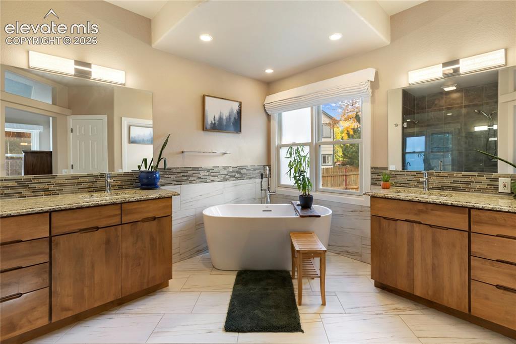 Image 9 of 38: Dual wood-finish vanities with light stone countertops, integrated sinks, a