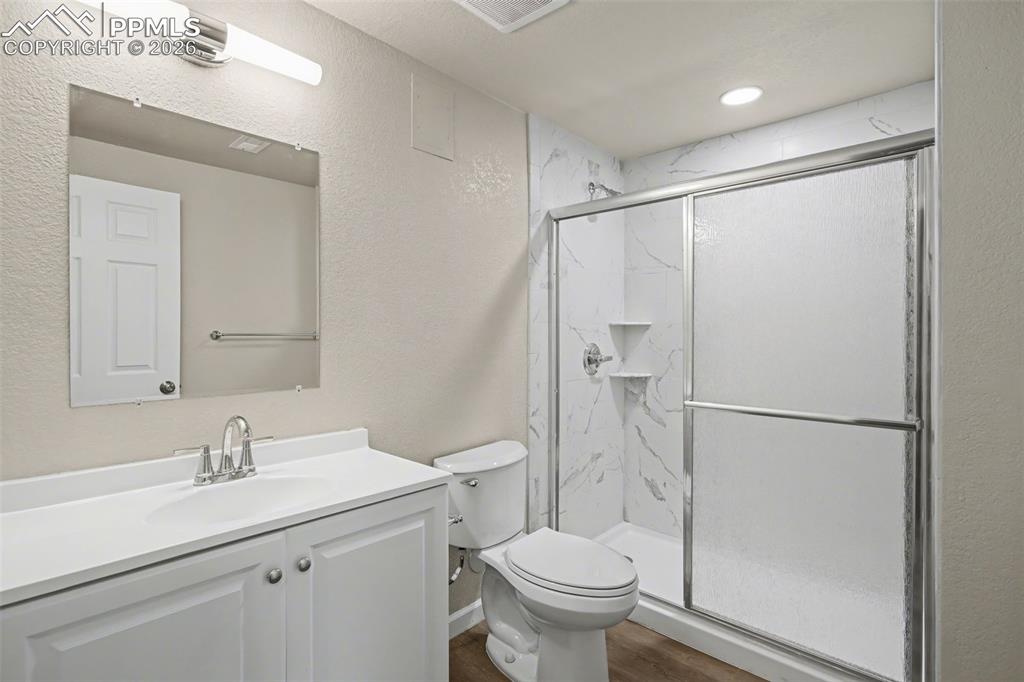 Image 38 of 40: Bathroom featuring a textured wall, vanity, a marble finish shower, dark wo