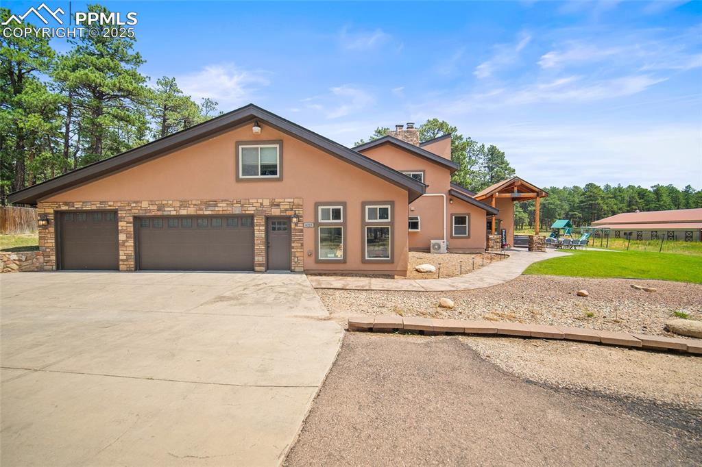 Caption: View of front of home featuring stucco siding, driveway, stone siding, a playground, and a chimney
