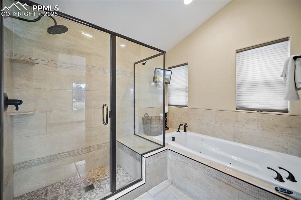 Image 20 of 47: Full bathroom with vaulted ceiling, a whirlpool tub, a stall shower, and re