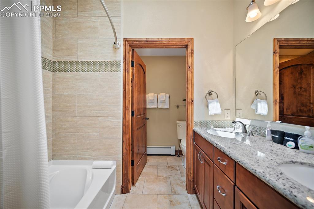 Image 30 of 47: Bathroom featuring double vanity, baseboard heating, and shower / bath comb