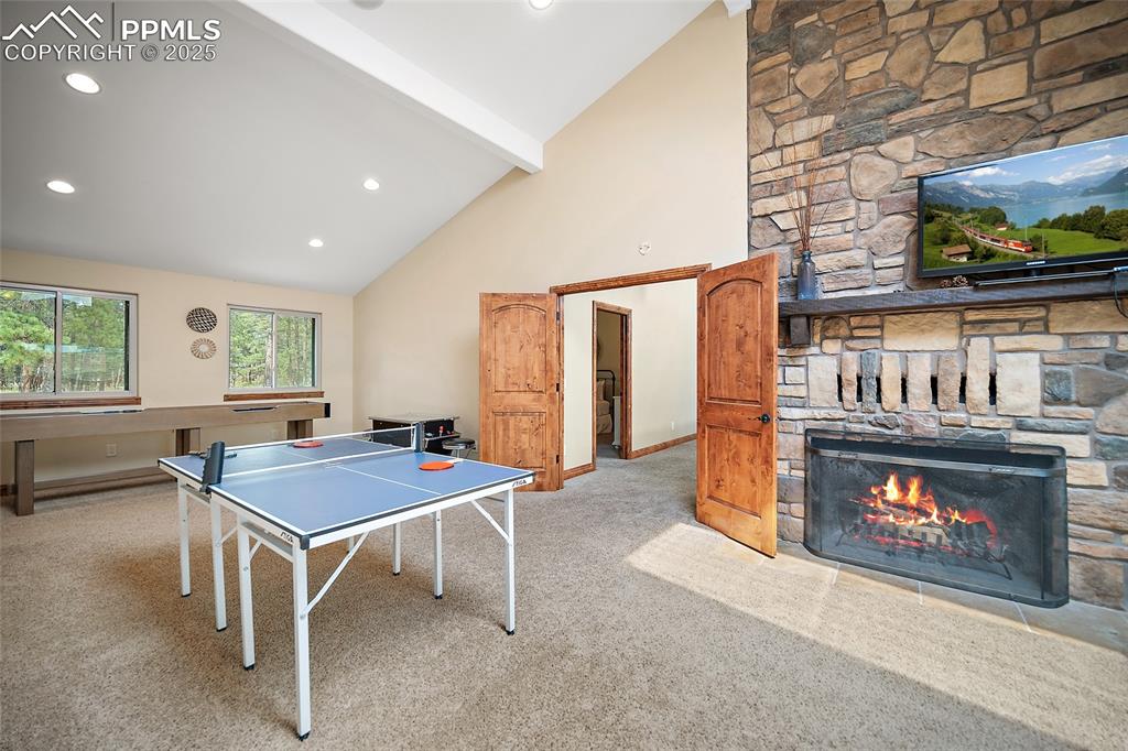 Image 34 of 47: Rec room with a fireplace, high vaulted ceiling, carpet, beamed ceiling, an