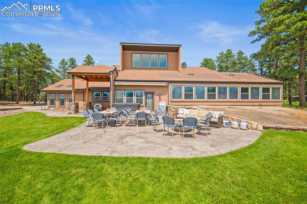 Image 38 of 47: Rear view of property featuring a shingled roof, a patio, a lawn, and stone