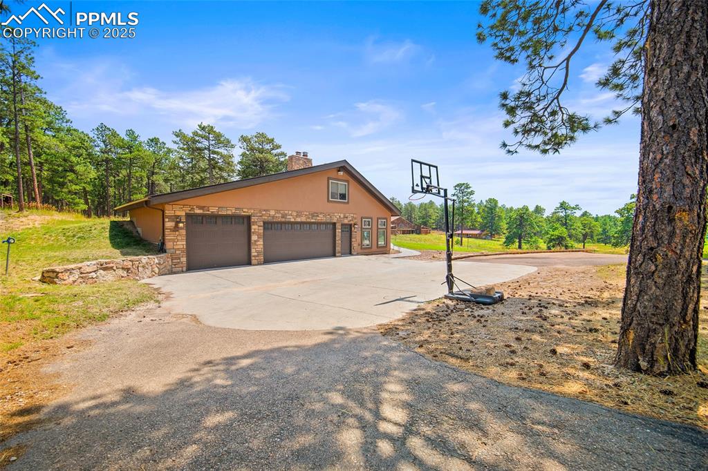 Image 39 of 47: View of side of home featuring driveway, a chimney, a garage, stone siding,