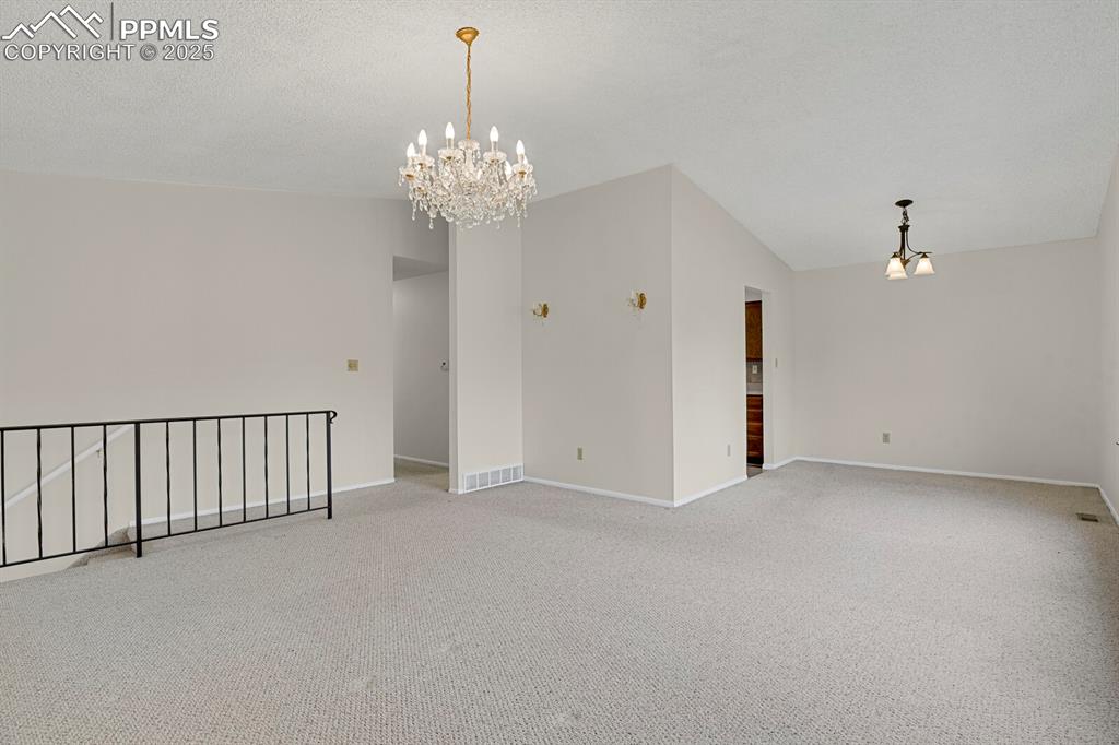 Image 10 of 45: Carpeted empty room with a chandelier, vaulted ceiling, and a textured ceil