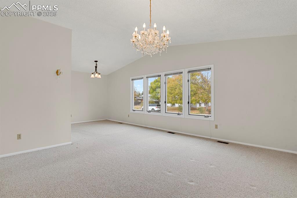 Image 11 of 45: Spare room featuring a chandelier, lofted ceiling, and carpet flooring