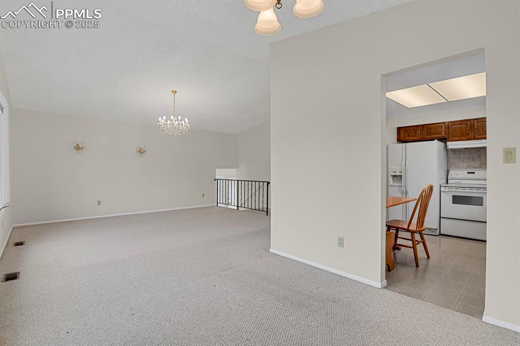Image 13 of 45: Spare room featuring a chandelier, light colored carpet, and a textured cei