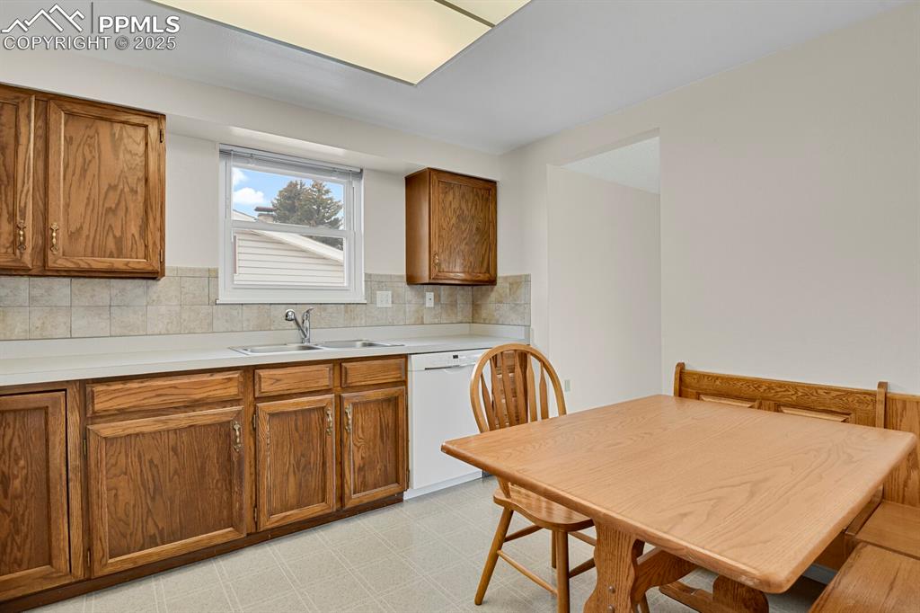 Image 15 of 45: Kitchen with brown cabinetry, light countertops, dishwasher, and decorative