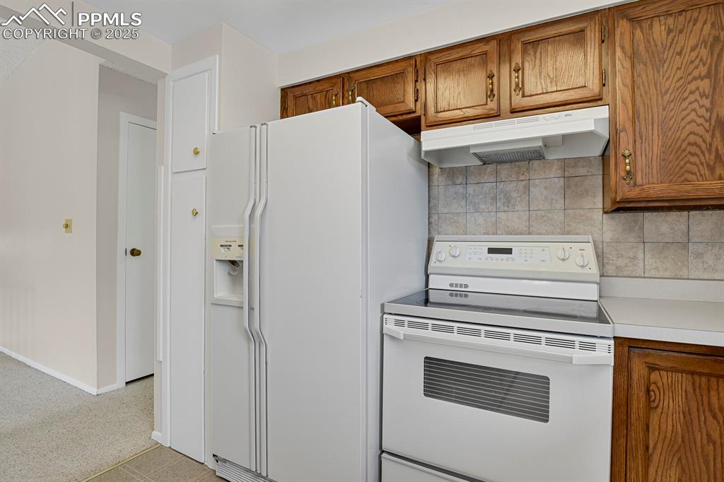 Image 17 of 45: Kitchen with white appliances, brown cabinets, light countertops, and under