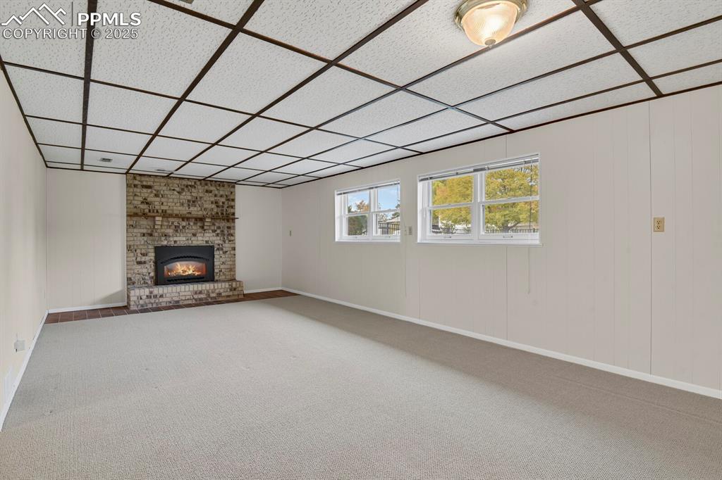 Image 27 of 45: Unfurnished living room featuring wood walls, carpet flooring, a brick fire