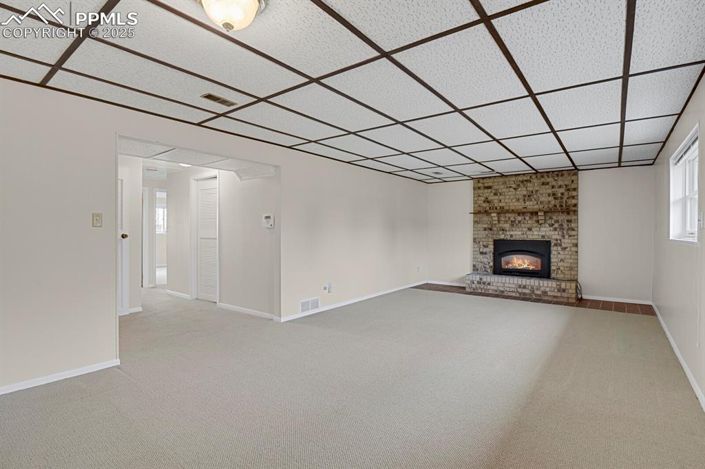 Image 28 of 45: Unfurnished living room with light carpet, a brick fireplace, and a drop ce