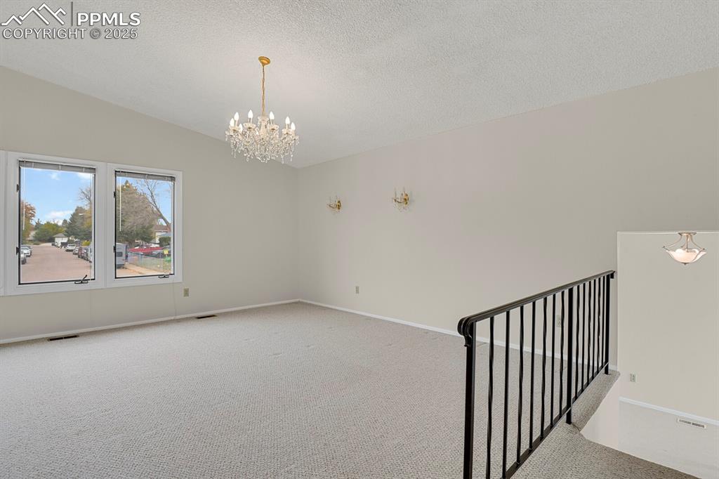 Image 7 of 45: Empty room with a chandelier, carpet, vaulted ceiling, and a textured ceili