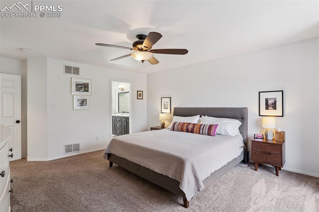 Image 19 of 40: Primary bedroom with light carpet, a ceiling fan, and connected bathroom