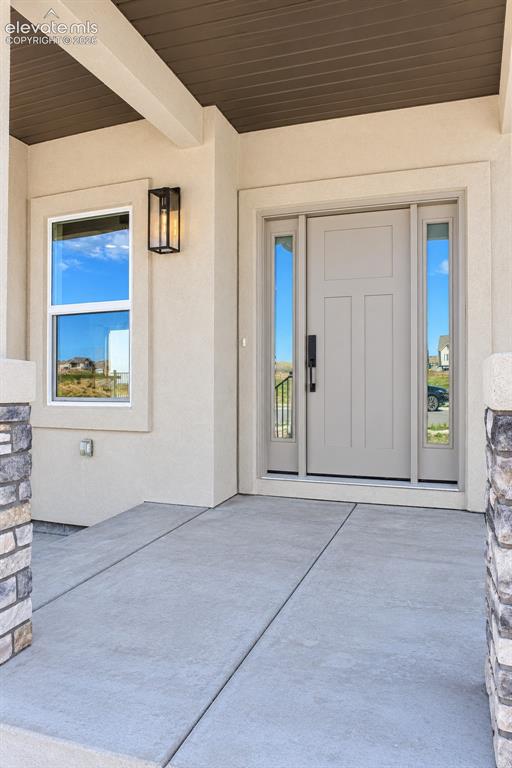 Image 6 of 44: Covered entry with concrete patio, stone column accents, and recessed wood-