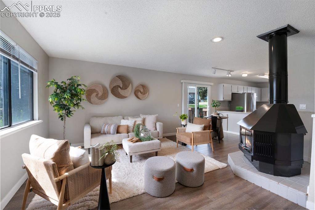 Image 2 of 26: Living room with a wood stove, wood finished floors, a textured ceiling, an