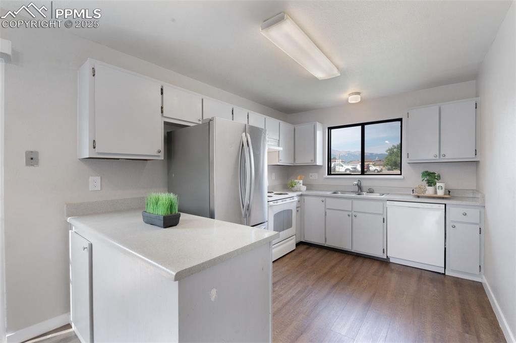 Image 8 of 26: Kitchen with white appliances, a peninsula, wood finished floors, and light