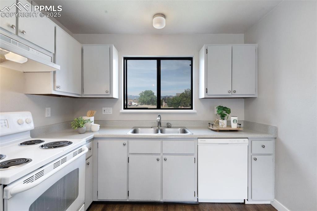 Image 9 of 26: Kitchen with white appliances, under cabinet range hood, light countertops,