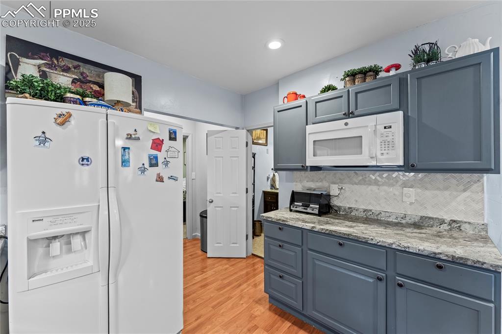 Image 9 of 27: Kitchen featuring white appliances, light wood-type flooring, tasteful back