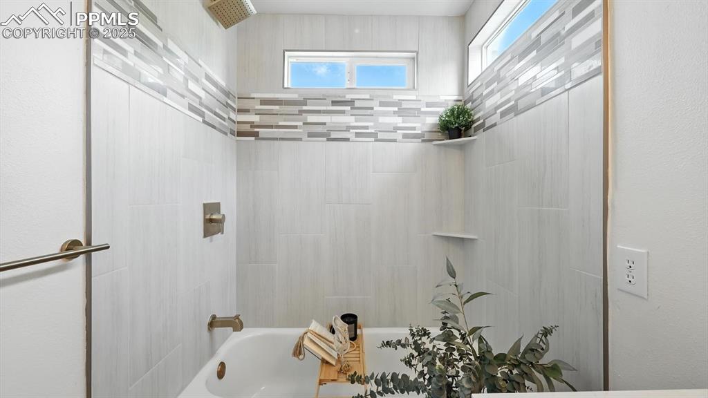 Image 37 of 50: Beautifully tiled tub/shower in the primary bathroom.
