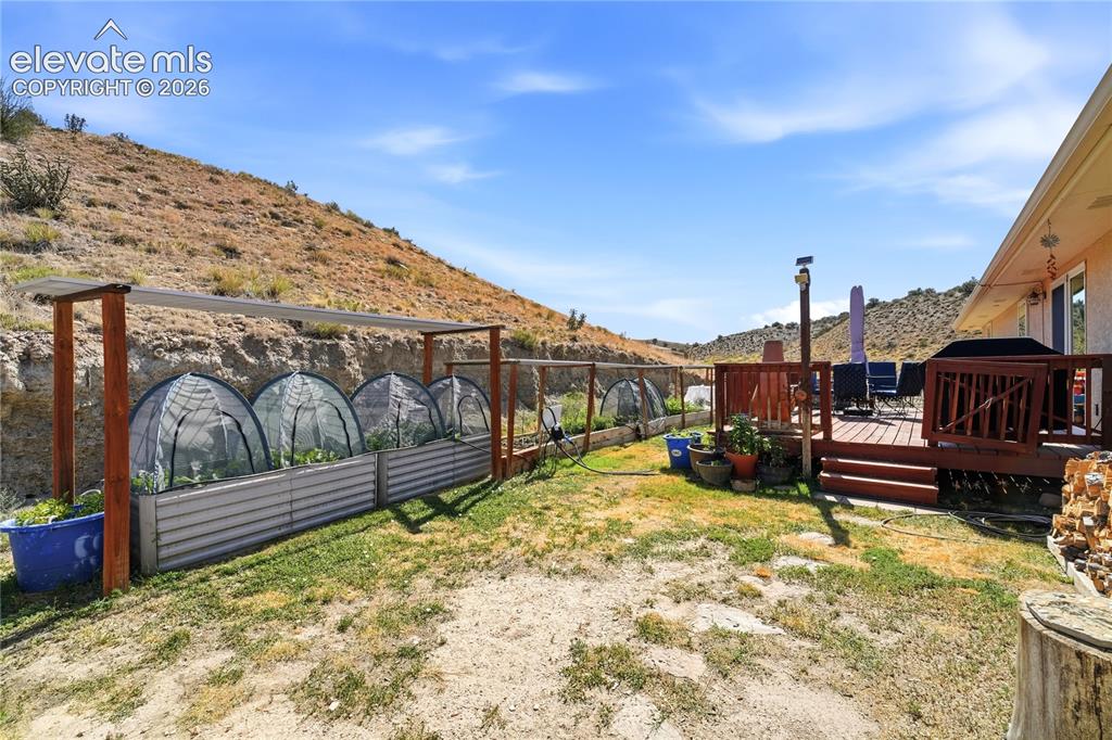Image 12 of 49: Expansive outdoor space featuring a wood deck, hillside backdrop, raised ga