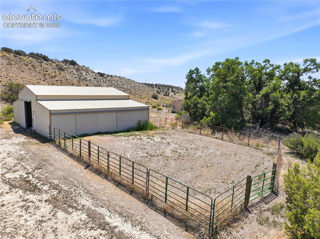 Image 15 of 49: Metal barn structure with a pitched roof, enclosed fenced area, and establi
