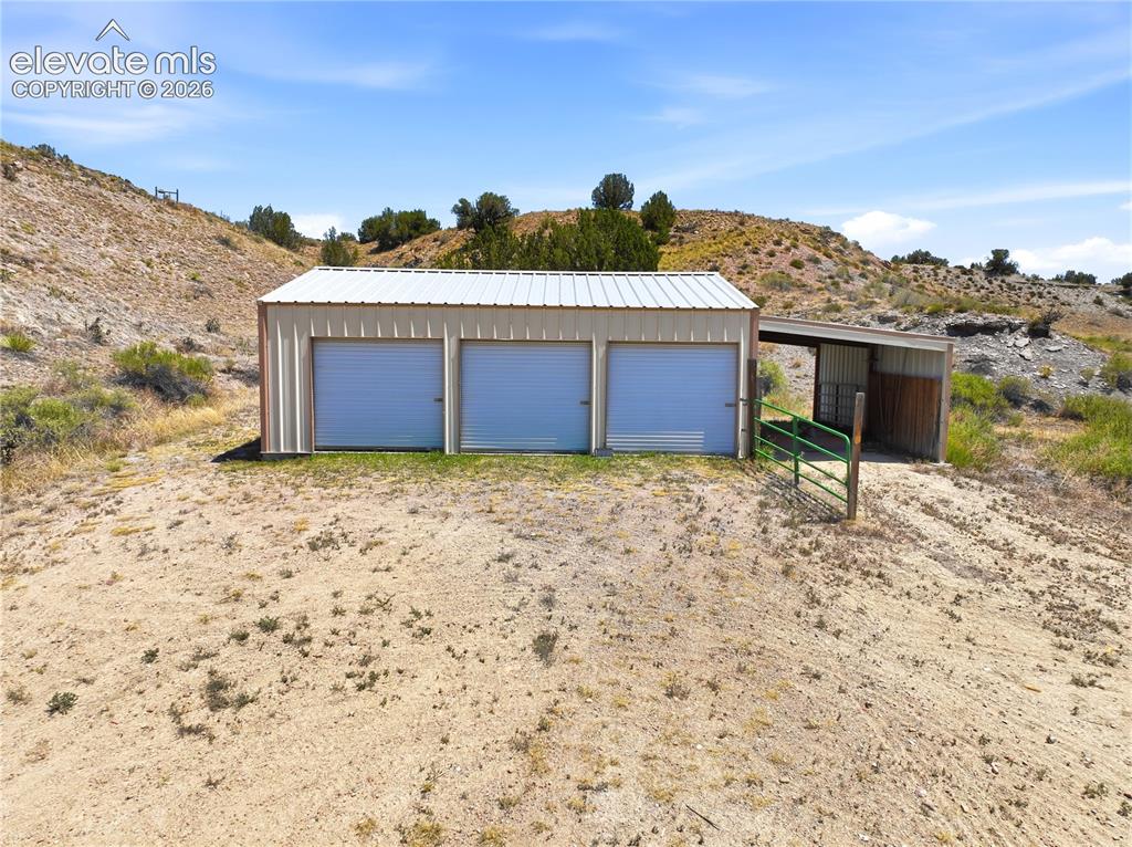 Image 20 of 49: Steel-clad outbuilding featuring three roll-up doors and an attached covere