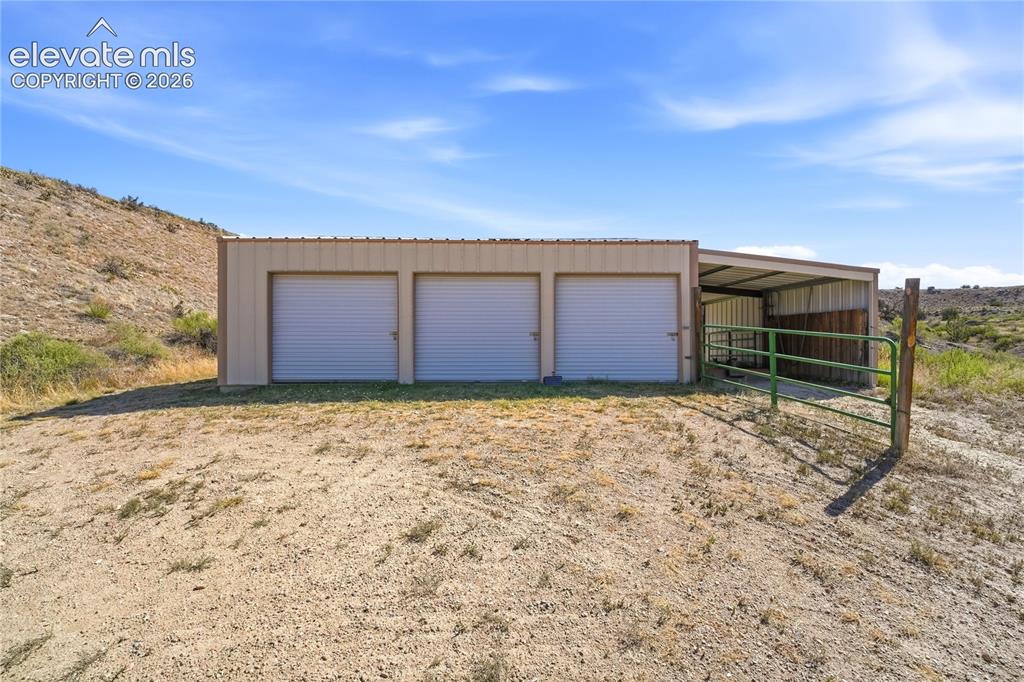 Image 21 of 49: Metal utility building featuring three roll-up doors, an open-sided shed ex