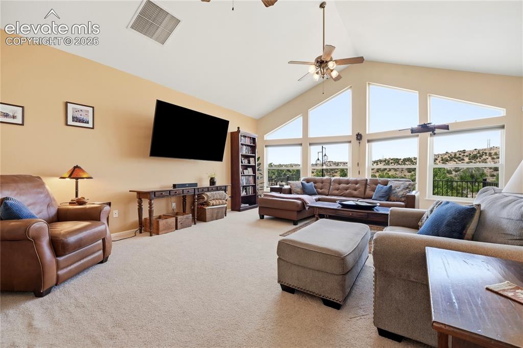 Image 25 of 49: Vaulted ceiling, expansive windows, ceiling fan, and carpeted flooring