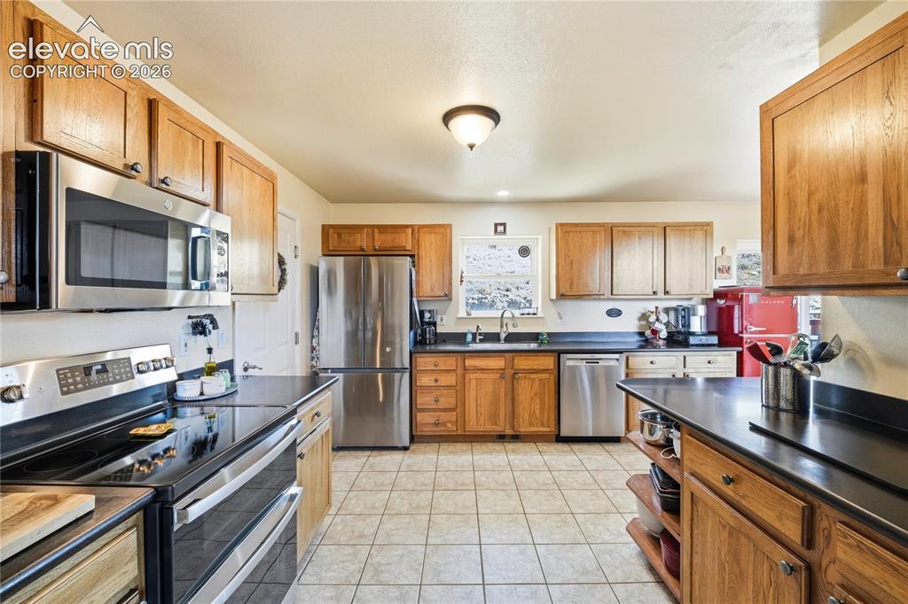 Image 27 of 49: Kitchen featuring tile flooring, wood cabinetry, stainless steel appliances