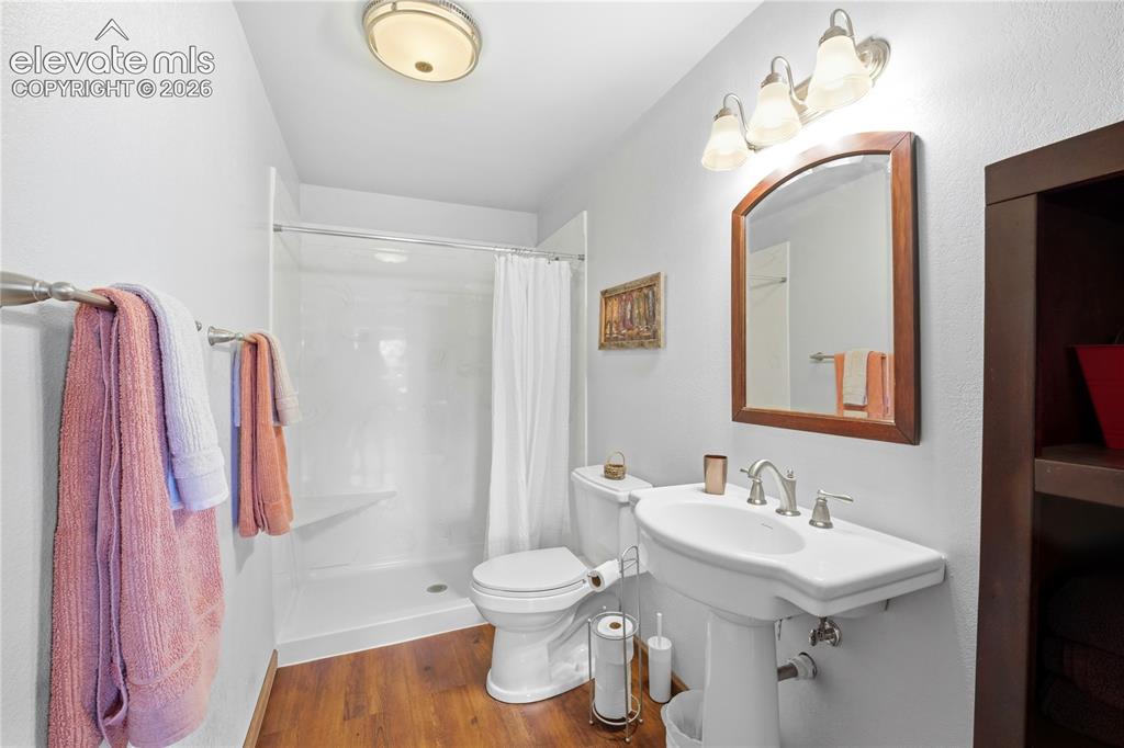 Image 45 of 49: Pedestal sink with chrome fixtures, wood-finish flooring, white shower with