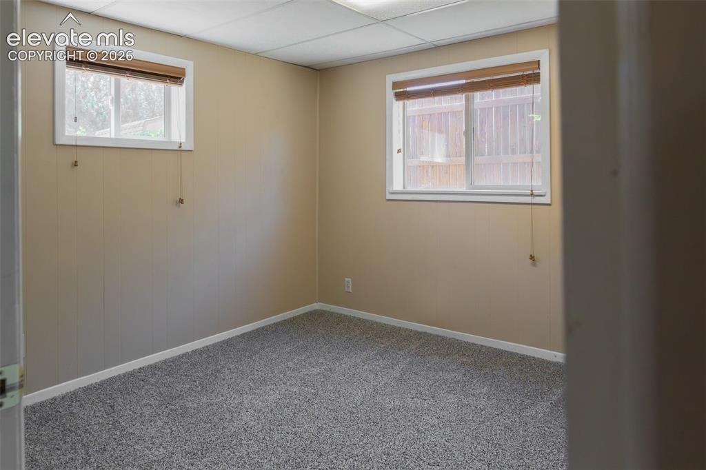 Image 29 of 38: Neutral tone wall paneling with white trim, two windows featuring wood blin