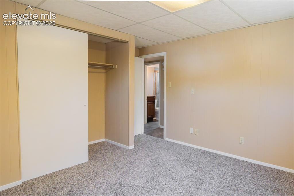 Image 34 of 38: Spacious room featuring neutral-toned walls, textured gray carpet, and a dr