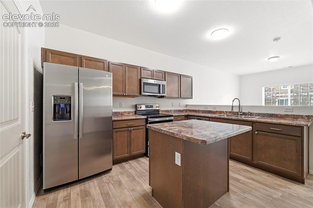 Image 15 of 44: Kitchen featuring wood-finish flooring, dark wood cabinetry, a central isla