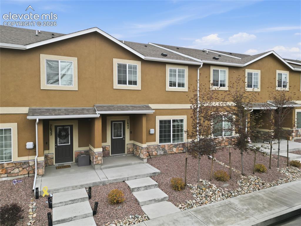Image 4 of 44: Townhome exterior featuring earth-toned stucco and stone veneer accents