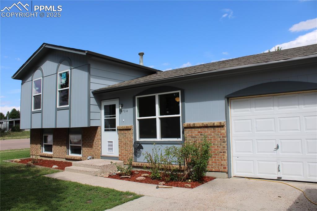 Caption: Split level home featuring brick siding, a shingled roof, a garage, and concrete driveway