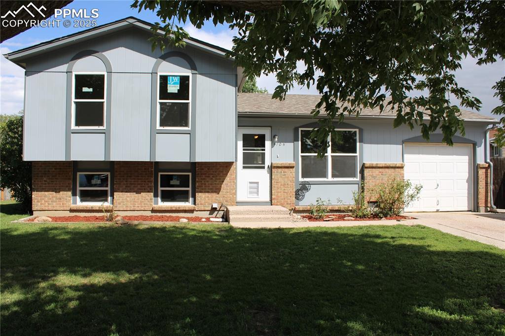 Image 2 of 35: Tri-level home featuring brick siding, a garage, a front yard, concrete dri