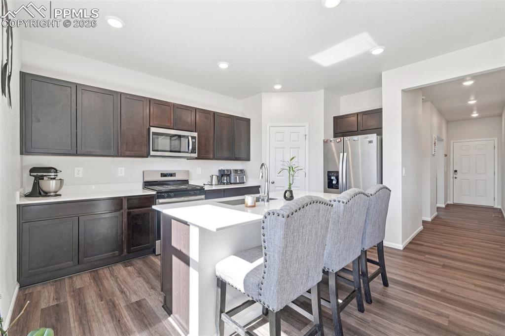 Image 5 of 34: Kitchen with stainless steel appliances, an island with sink, dark wood-sty