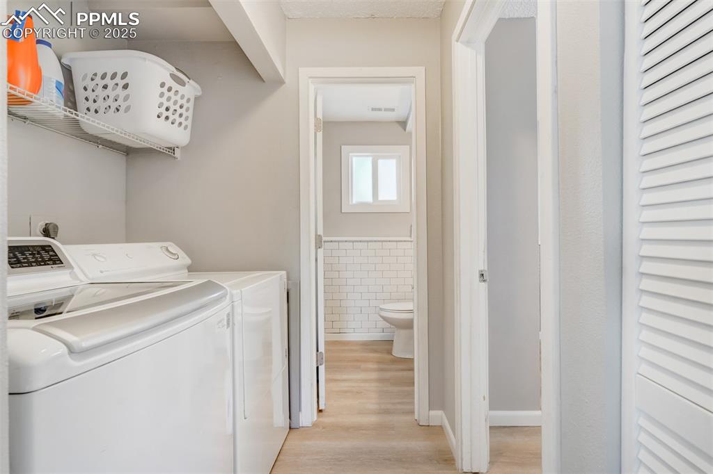 Image 24 of 25: Laundry area featuring tile walls, light wood finished floors, washer and c