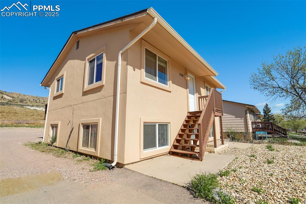 Image 3 of 25: Rear view of house with stucco siding, stairs, and a patio