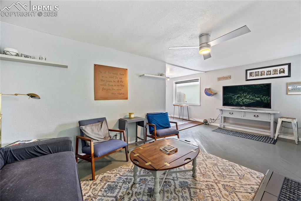 Image 13 of 36: Living room with ceiling fan, a textured ceiling, baseboards, and wood fini