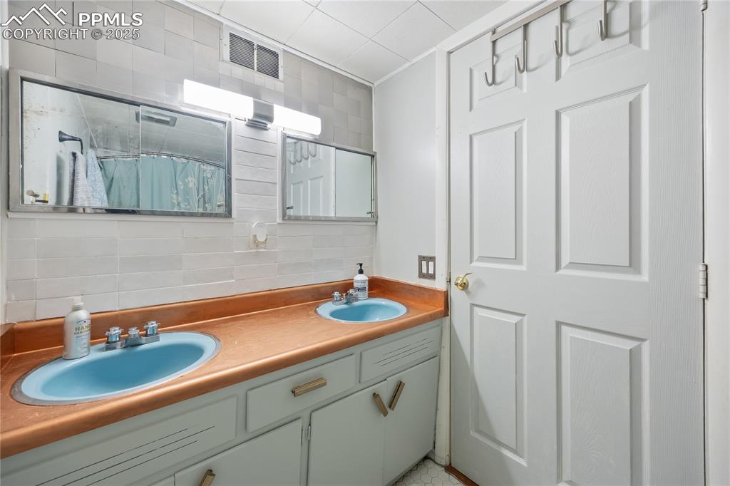 Image 26 of 36: Bathroom featuring double vanity, visible vents, decorative backsplash, and