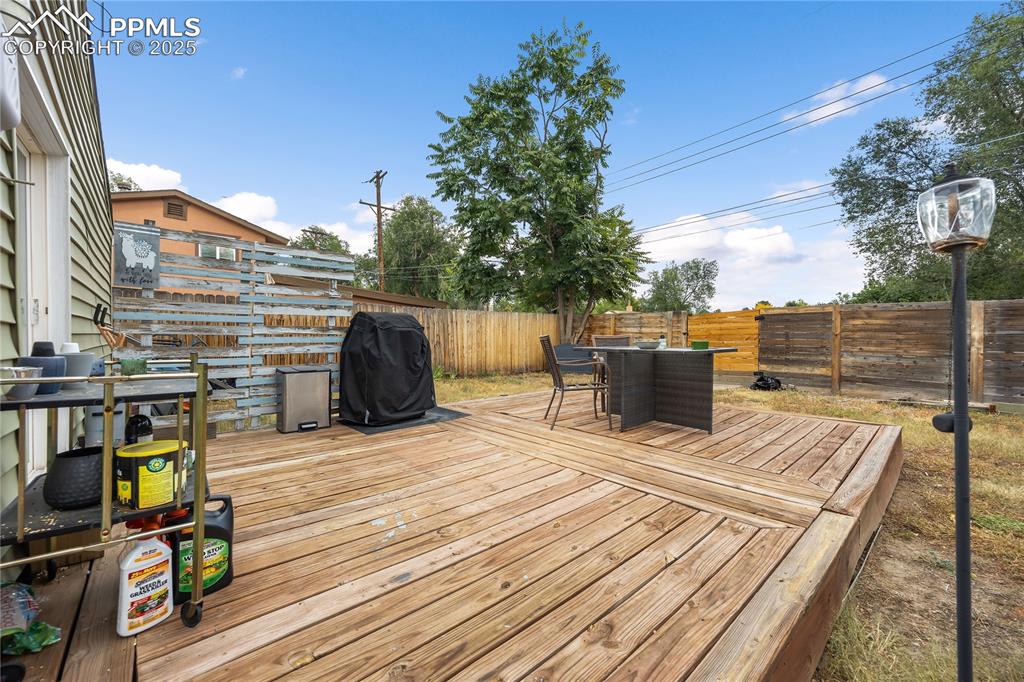 Image 32 of 36: Wooden deck with outdoor dining area, a fenced backyard, and a grill