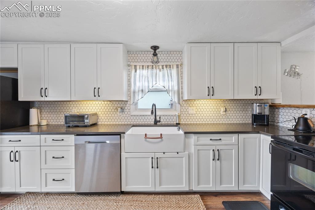 Image 4 of 36: Kitchen with electric range, white cabinets, dark countertops, stainless st